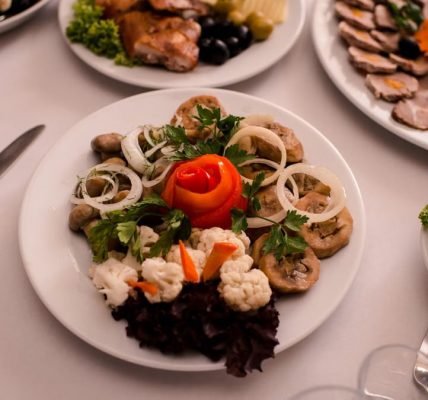 Beautifully arranged gourmet plates with meats, cheeses, and garnishes on a white table setting.