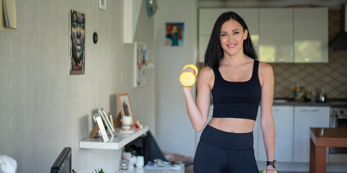 Smiling woman in activewear lifting dumbbells at home for a healthy lifestyle.