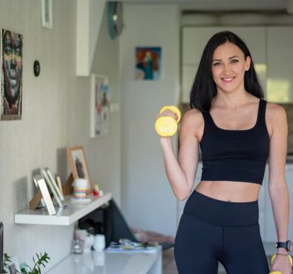 Smiling woman in activewear lifting dumbbells at home for a healthy lifestyle.